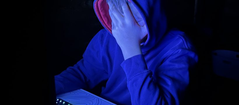 Jugendlicher sitzt im Kaputzenpulli vor PC-Bildschrim.